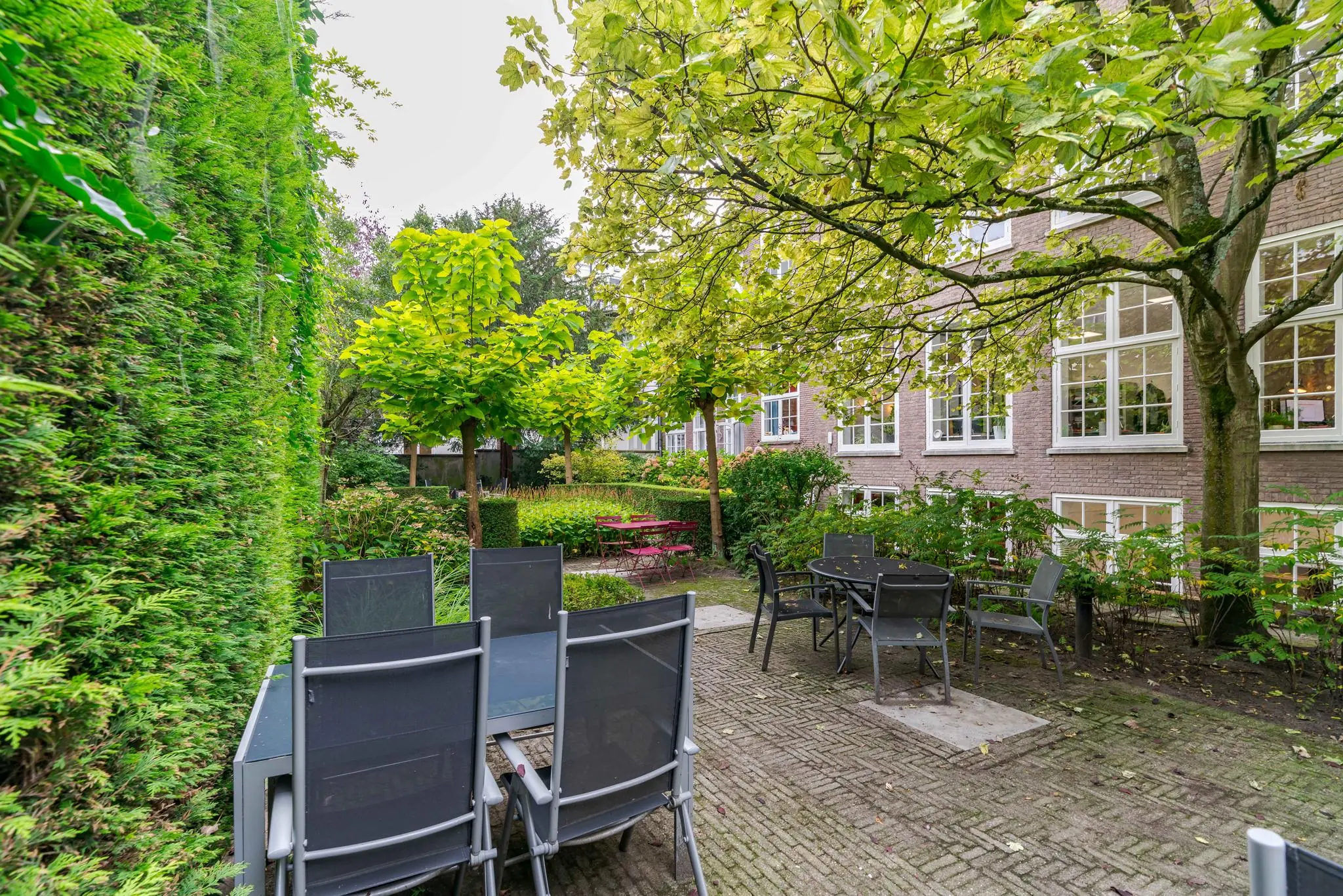 Binnentuin met terrasmeubilair, omgeven door groen en een woongebouw aan het Lange Voorhout.